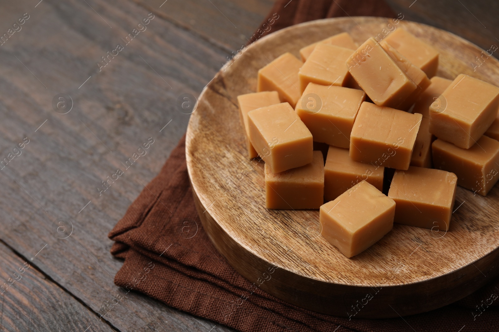 Photo of Tasty sweet caramel candies on wooden table, closeup. Space for text