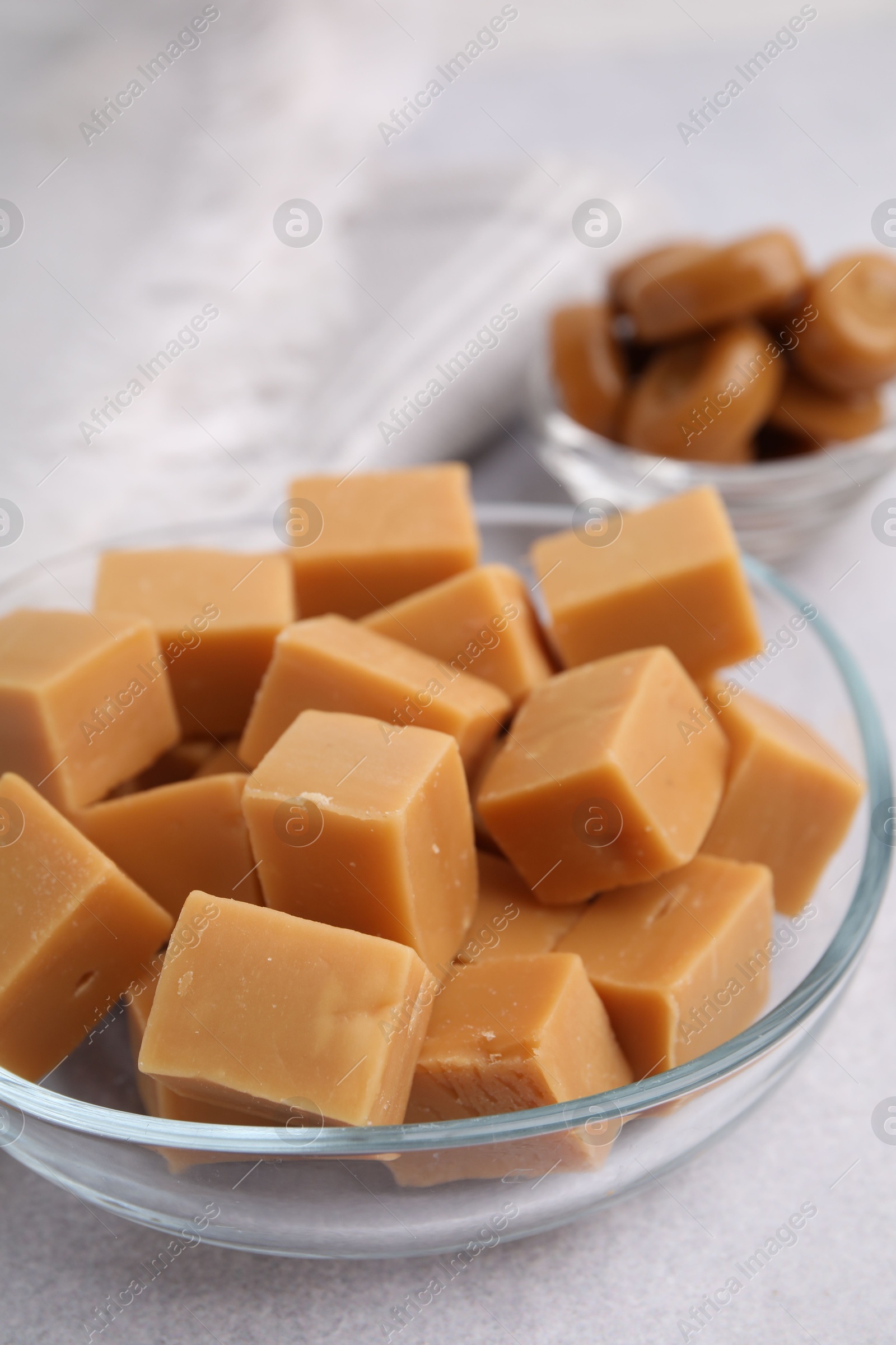 Photo of Tasty sweet caramel candies in bowl on light table, closeup