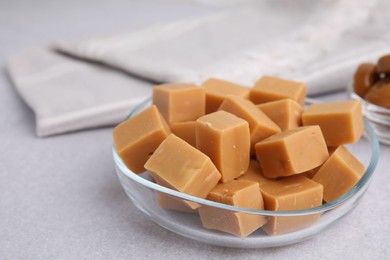 Photo of Tasty sweet caramel candies in bowl on light grey table, closeup