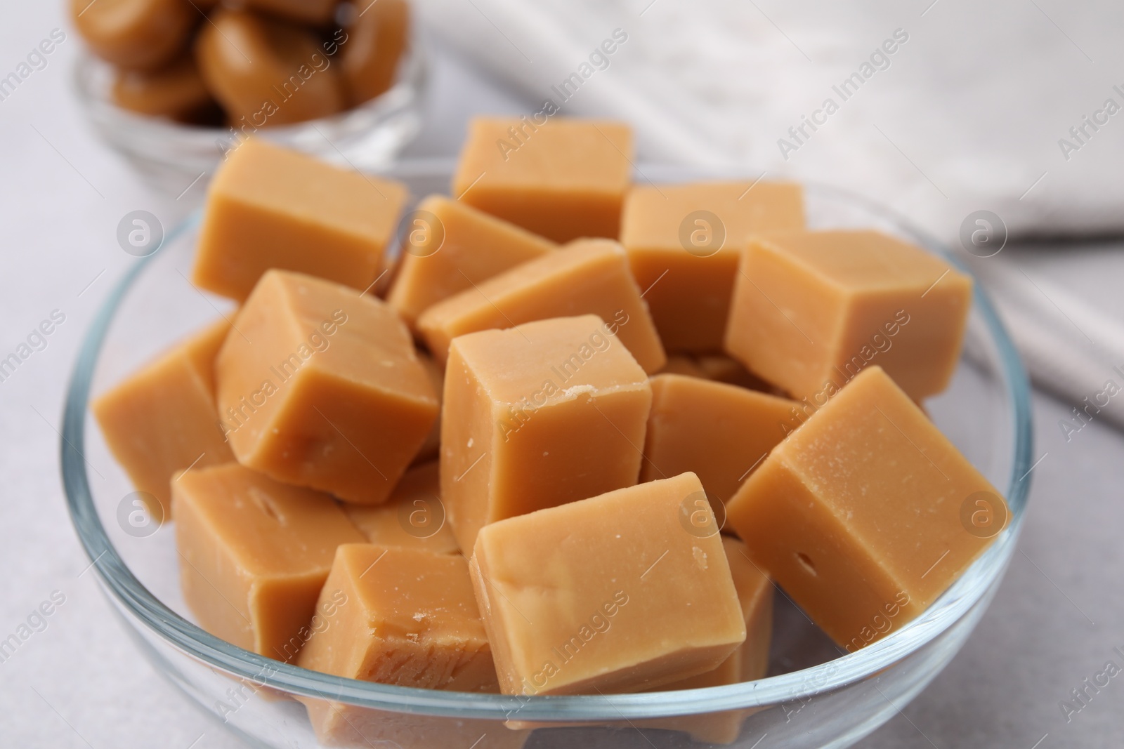 Photo of Tasty sweet caramel candies in bowl on light table, closeup