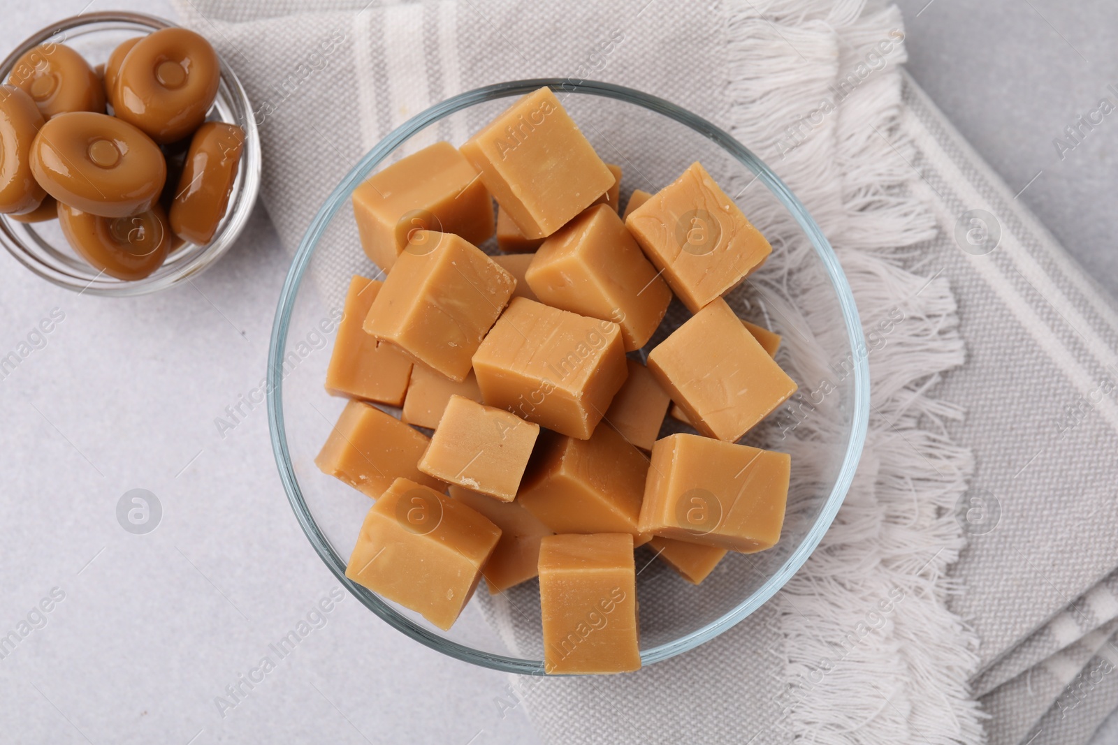 Photo of Tasty sweet caramel candies in bowls on light grey table, flat lay