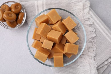 Photo of Tasty sweet caramel candies in bowls on light grey table, flat lay