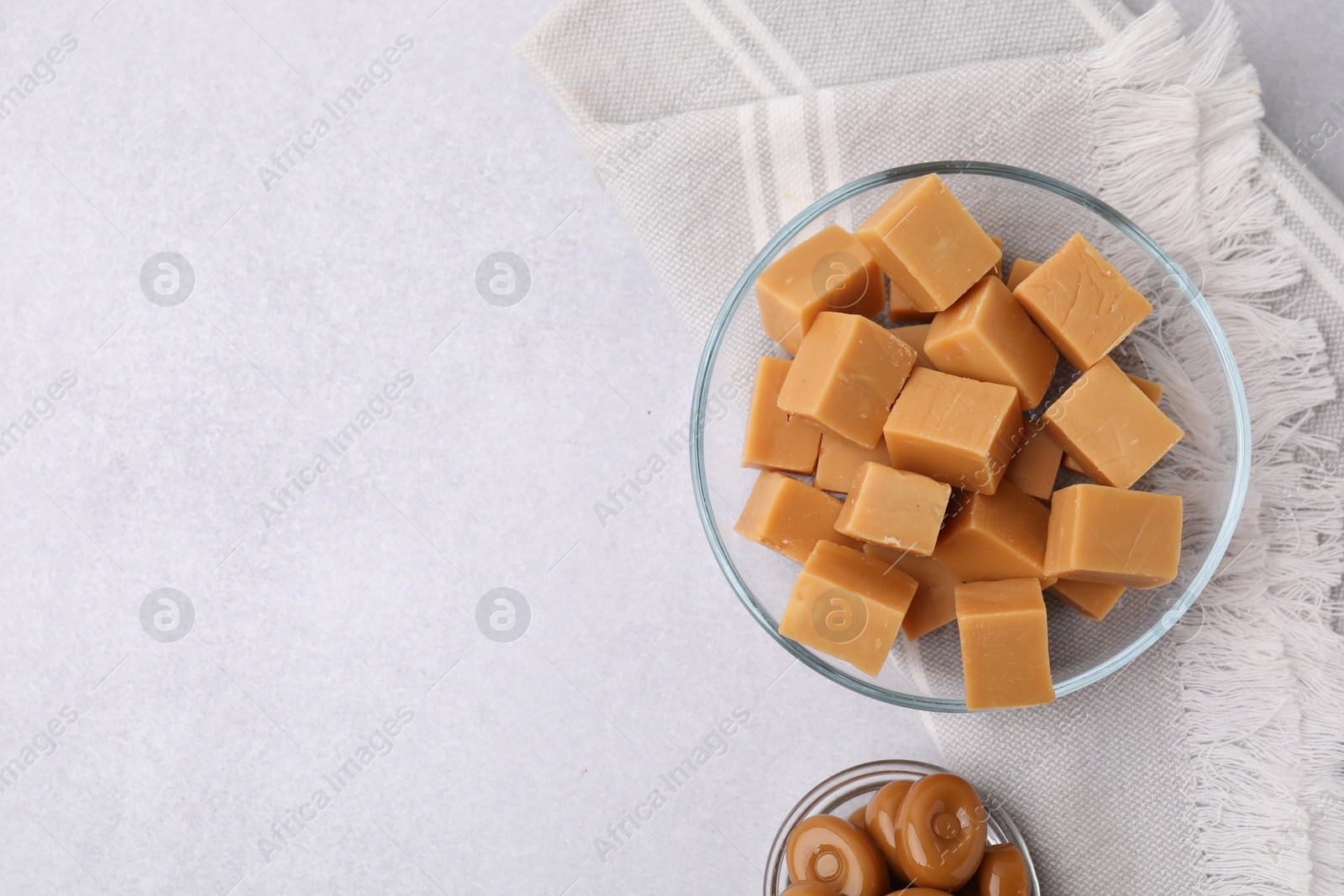 Photo of Tasty sweet caramel candies in bowls on light grey table, flat lay. Space for text