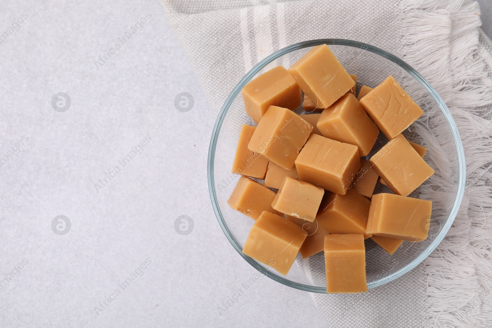 Photo of Tasty sweet caramel candies in bowl on light grey table, top view. Space for text