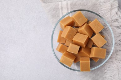 Photo of Tasty sweet caramel candies in bowl on light grey table, top view. Space for text