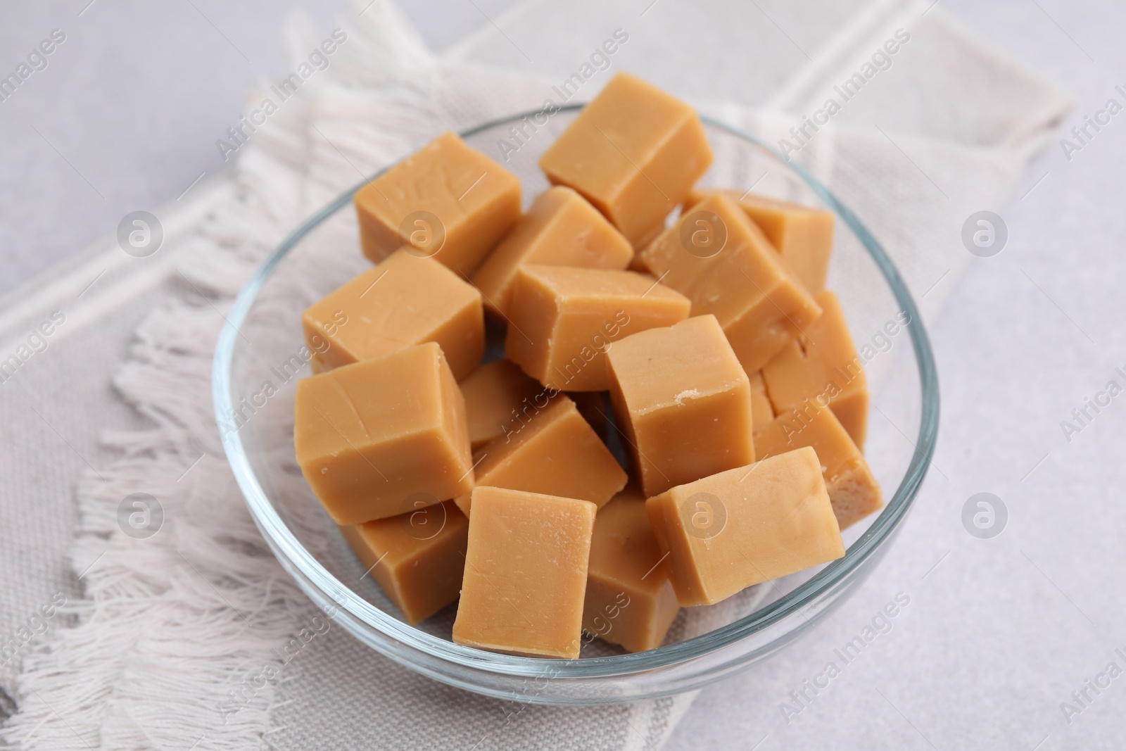 Photo of Tasty sweet caramel candies in bowl on light grey table, closeup