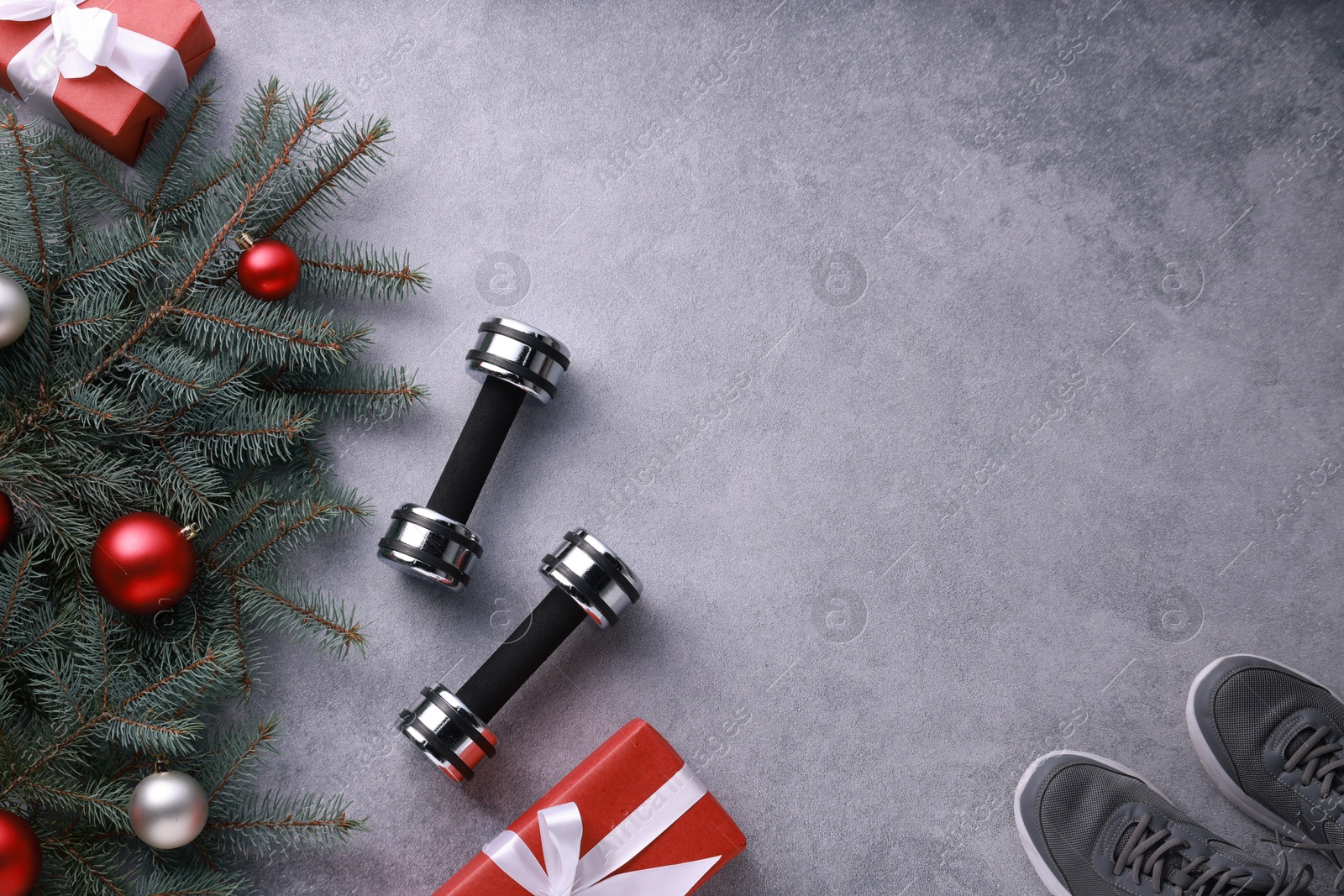 Photo of Dumbbells, gift boxes, fitness mat, sneakers and Christmas decor on grey background, flat lay. Space for text