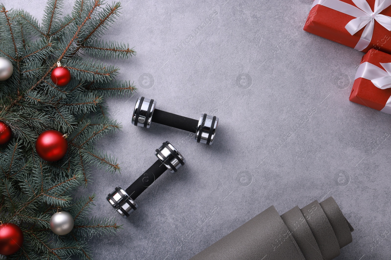 Photo of Dumbbells, gift boxes, fitness mat, sneakers and Christmas decor on grey background, flat lay