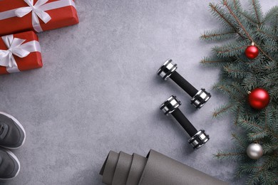 Photo of Dumbbells, gift boxes, fitness mat, sneakers and Christmas decor on grey background, flat lay. Space for text