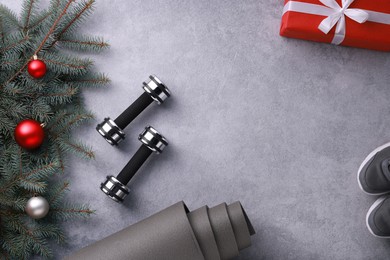 Photo of Dumbbells, gift box, fitness mat, sneakers and Christmas decor on grey background, flat lay. Space for text