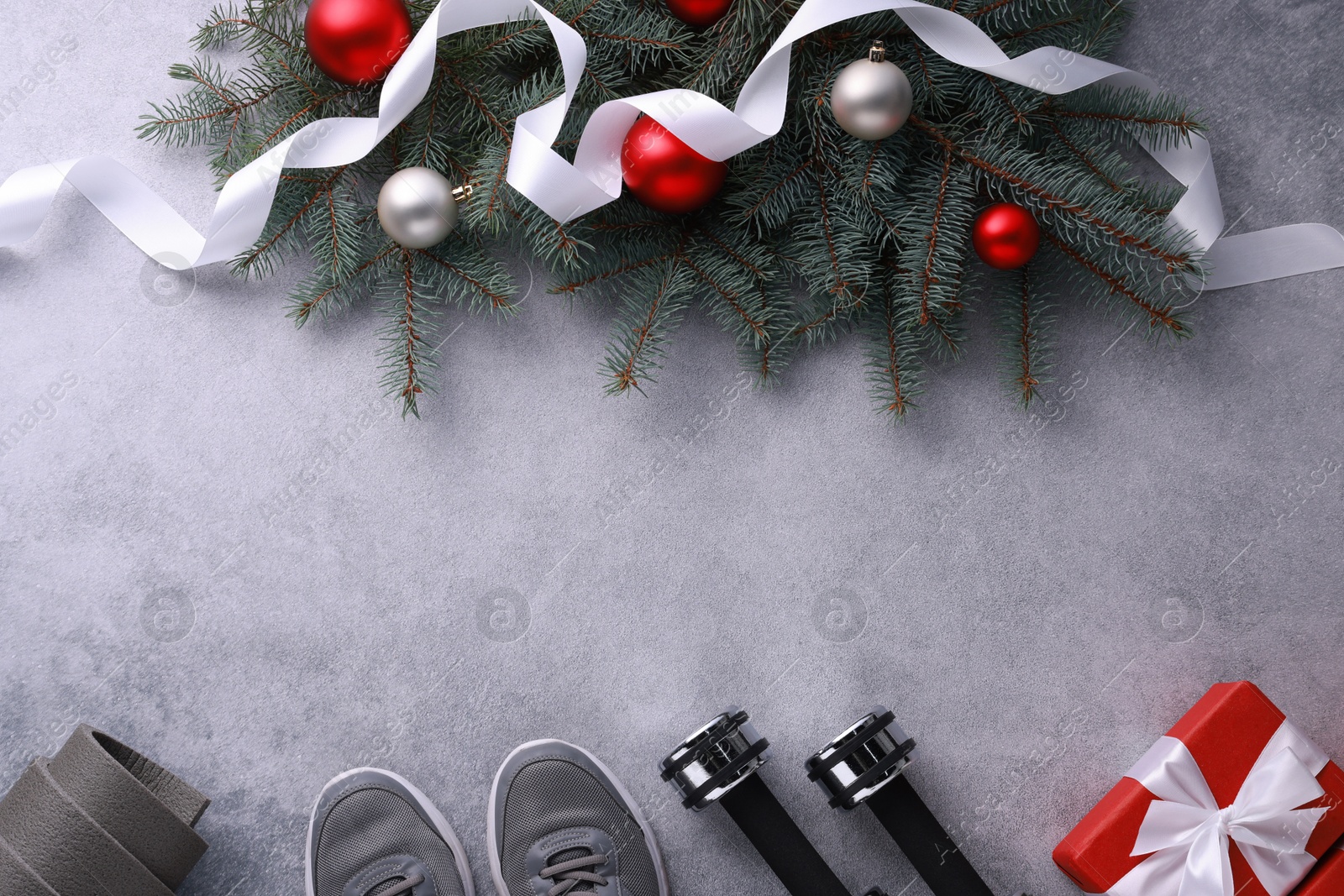 Photo of Dumbbells, gift box, fitness mat, sneakers and Christmas decor on grey background, flat lay. Space for text