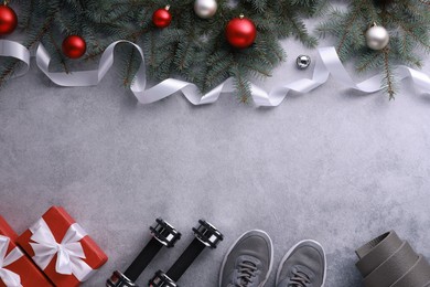 Photo of Dumbbells, gift boxes, fitness mat, sneakers and Christmas decor on grey background, flat lay. Space for text