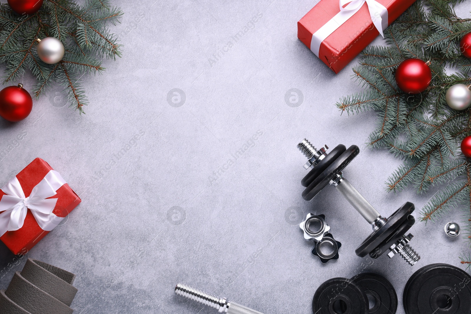 Photo of Barbell, gift boxes, fitness mat and Christmas decor on grey background, flat lay. Space for text