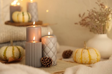 Burning candles, pumpkins and cones near beige wall. Autumn atmosphere