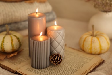 Burning candles, pumpkins and cone on book indoors, closeup. Autumn atmosphere