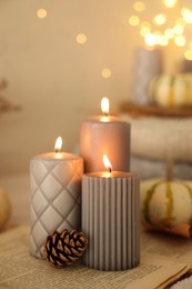 Burning candles and cone on book indoors. Autumn atmosphere