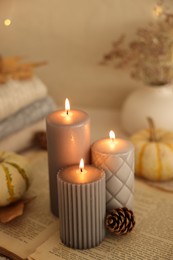 Burning candles and cone on book indoors. Autumn atmosphere