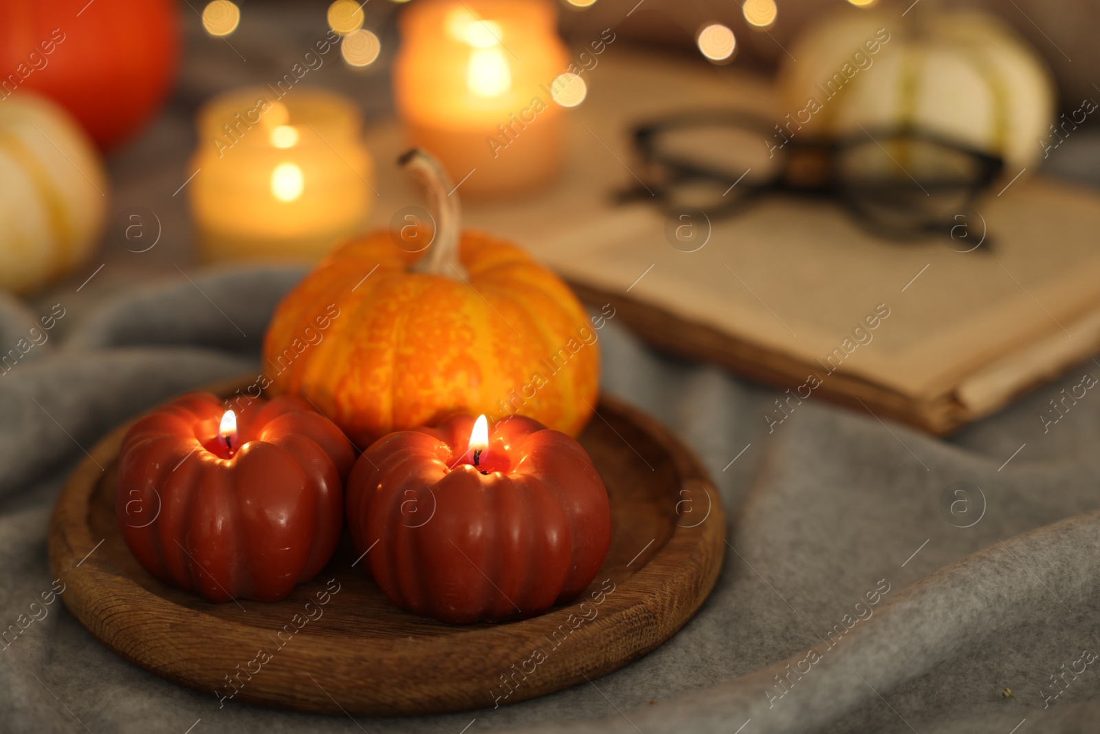 Photo of Burning candles and pumpkin on grey cloth against blurred lights, closeup. Autumn atmosphere