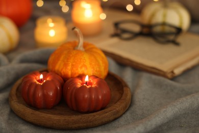 Burning candles and pumpkin on grey cloth against blurred lights, closeup. Autumn atmosphere