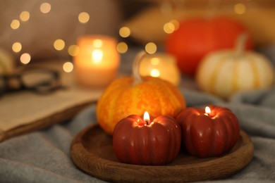 Photo of Burning candles and pumpkin on grey cloth against blurred lights, closeup. Autumn atmosphere