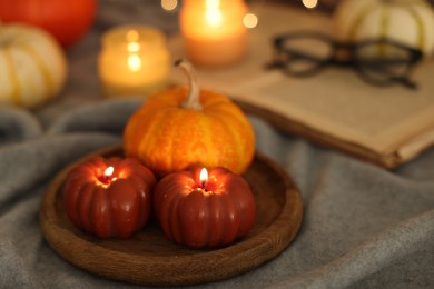 Burning candles on grey cloth against blurred lights, closeup. Autumn atmosphere