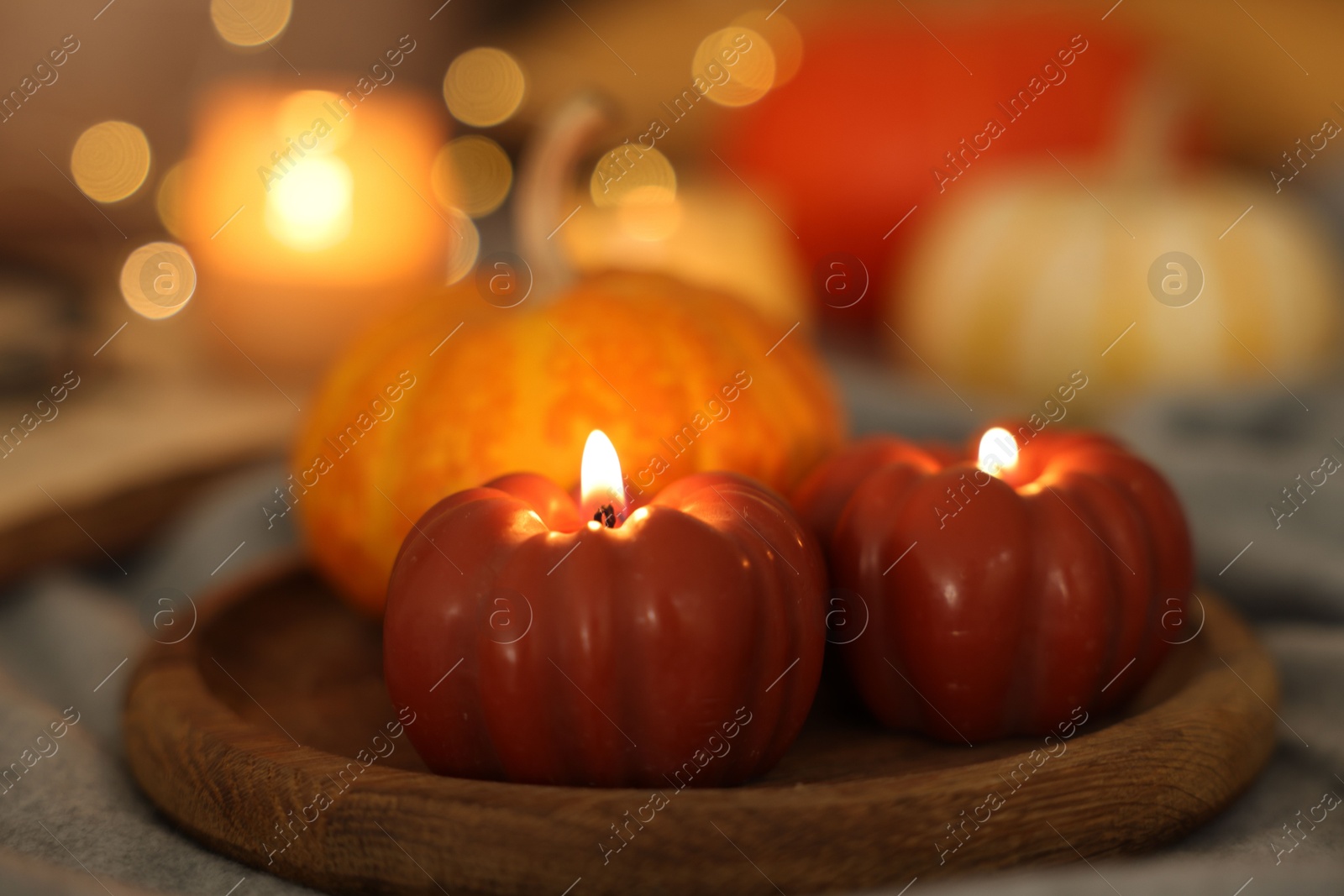 Photo of Burning candles and pumpkin on grey cloth against blurred lights, closeup. Autumn atmosphere