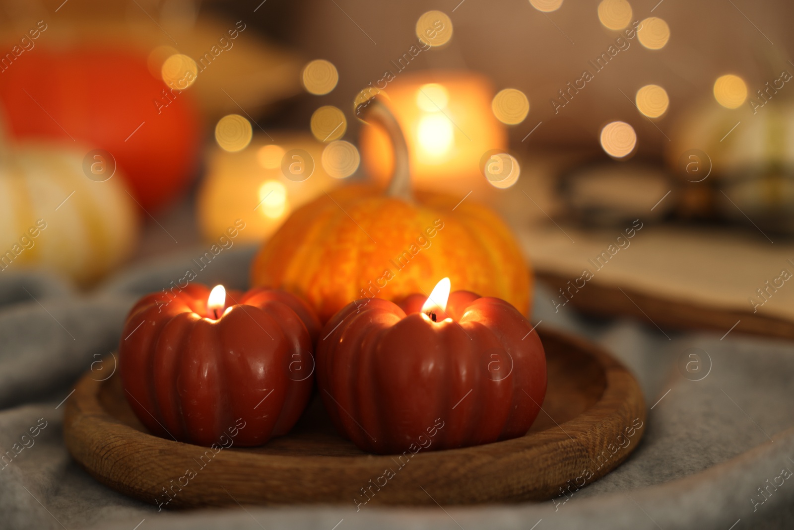 Photo of Burning candles and pumpkin on grey cloth against blurred lights, closeup. Autumn atmosphere