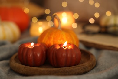 Photo of Burning candles and pumpkin on grey cloth against blurred lights, closeup. Autumn atmosphere