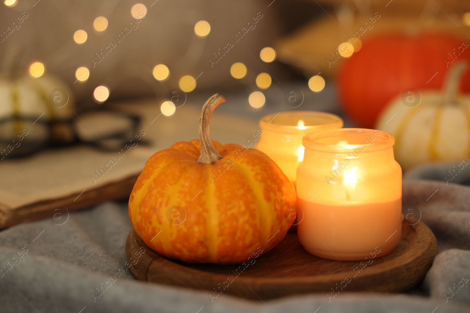 Photo of Burning candles and pumpkin on grey cloth against blurred lights, closeup. Autumn atmosphere