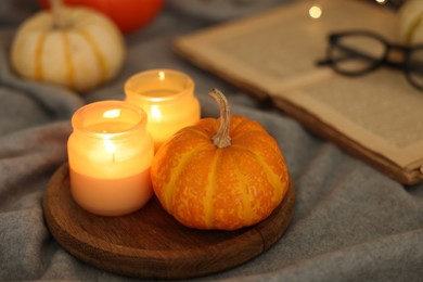 Photo of Burning candles and pumpkin on grey cloth, closeup. Autumn atmosphere