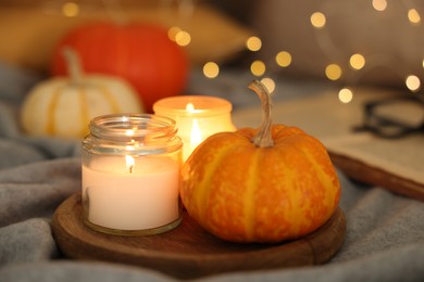 Burning candles and pumpkin on grey cloth against blurred lights, closeup. Autumn atmosphere