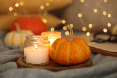 Photo of Burning candles and pumpkin on grey cloth against blurred lights, closeup. Autumn atmosphere