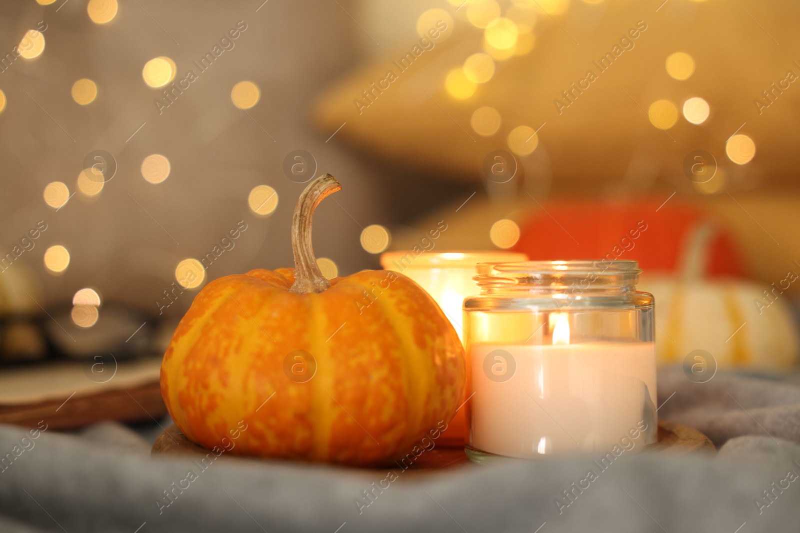 Photo of Burning candles and pumpkin on grey cloth against blurred lights, closeup. Autumn atmosphere