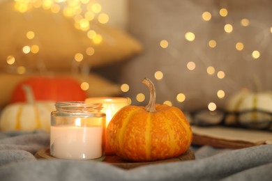 Photo of Burning candles and pumpkin on grey cloth against blurred lights, closeup. Autumn atmosphere