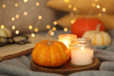 Photo of Burning candles and pumpkin on grey cloth against blurred lights, closeup. Autumn atmosphere