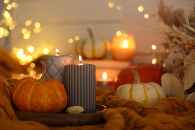 Photo of Burning candles and pumpkins on soft sweater indoors, closeup. Autumn atmosphere