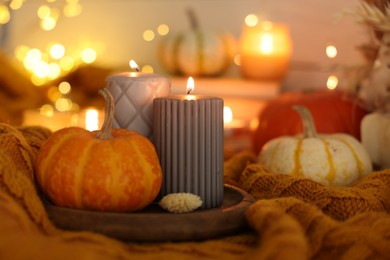 Photo of Burning candles and pumpkins on soft sweater indoors, closeup. Autumn atmosphere