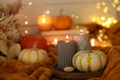 Photo of Burning candles and pumpkins on soft sweater indoors, closeup. Autumn atmosphere