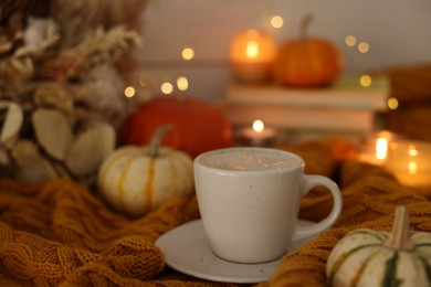 Photo of Cup of coffee and pumpkins on soft sweater, closeup. Autumn atmosphere