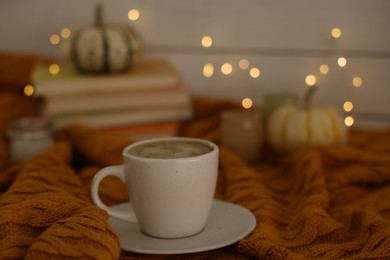 Photo of Cup of coffee on soft sweater, closeup. Autumn atmosphere