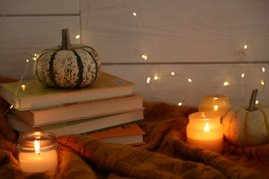 Photo of Burning candles, stack of books, festive lights and pumpkins on soft sweater indoors. Autumn atmosphere