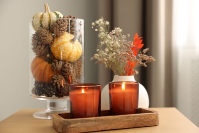 Photo of Burning candles and autumn decor on wooden table indoors, closeup