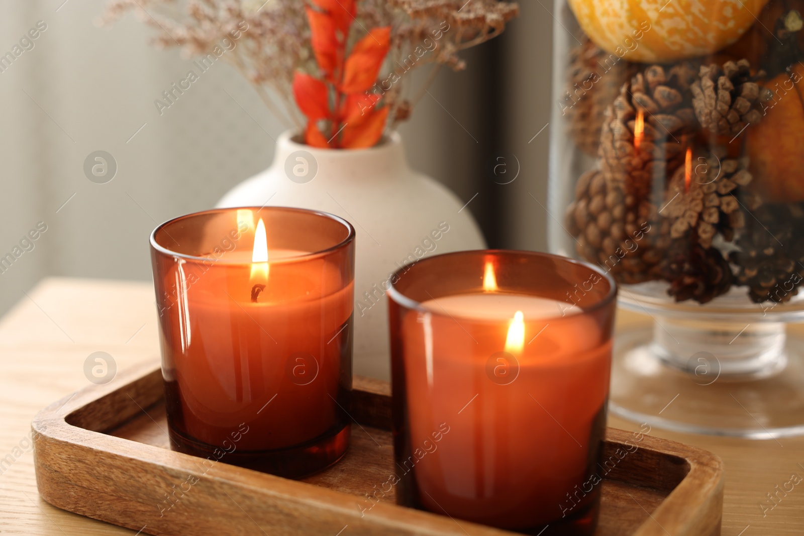 Photo of Burning candles and autumn decor on wooden table indoors, closeup