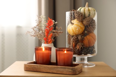 Photo of Burning candles and autumn decor on wooden table indoors, closeup