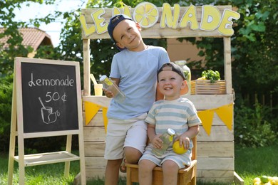 Photo of Cute boys with refreshing drinks near lemonade stand in park