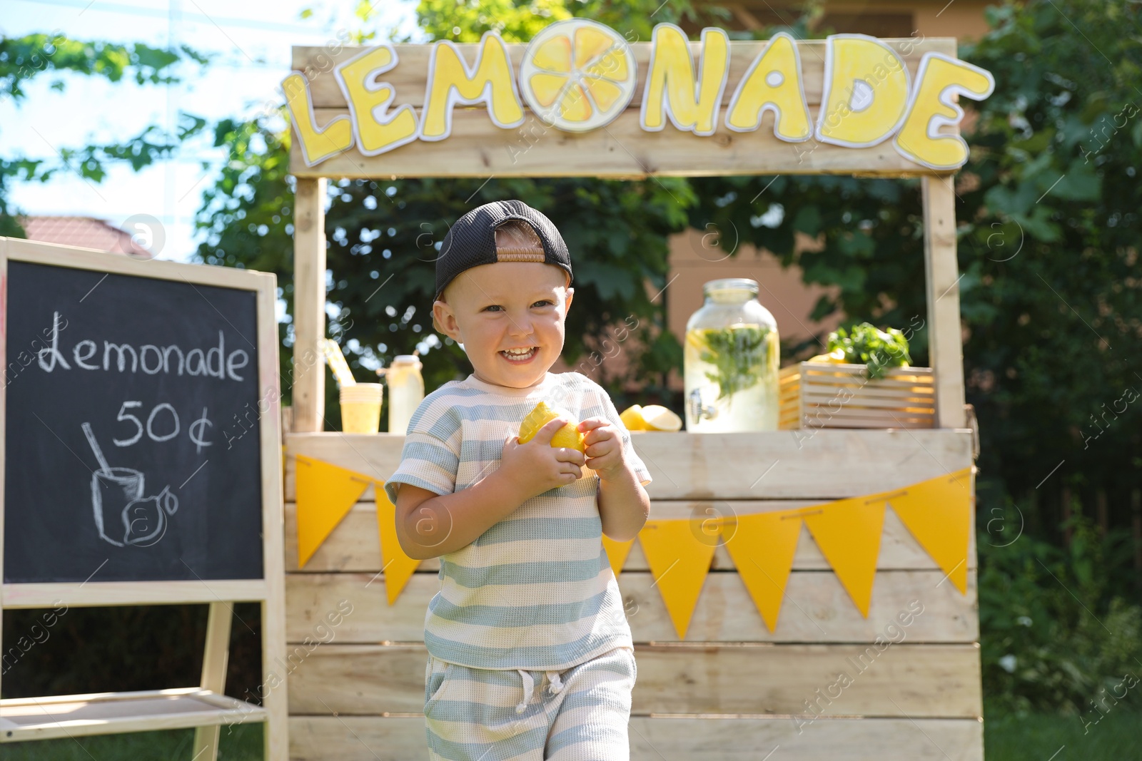 Photo of Cute little boy with fresh fruit near lemonade stand in park