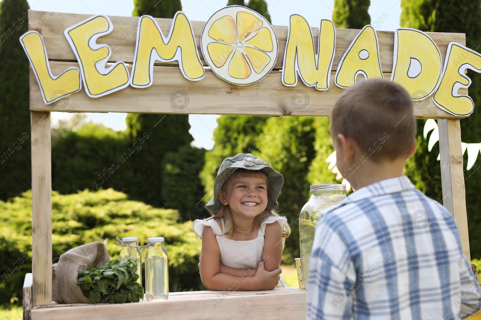 Photo of Cute little girl selling natural lemonade to boy in park