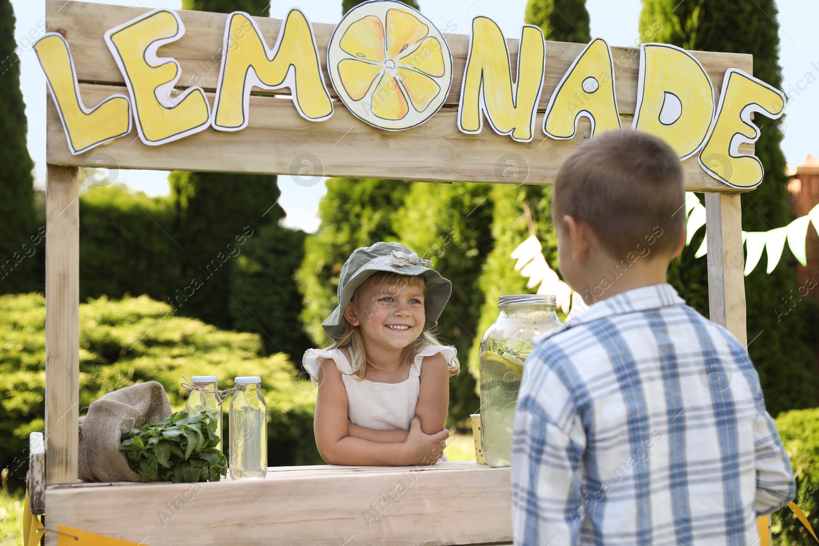 Photo of Cute little girl selling natural lemonade to boy in park