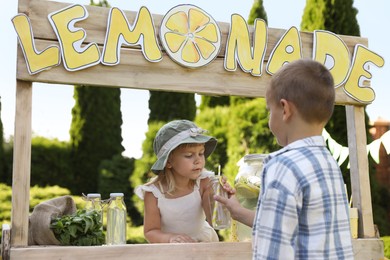 Photo of Cute little girl selling natural lemonade to boy in park