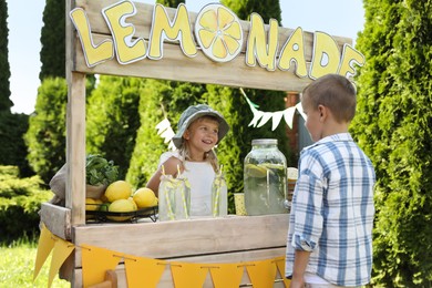 Photo of Cute little girl selling natural lemonade to boy in park